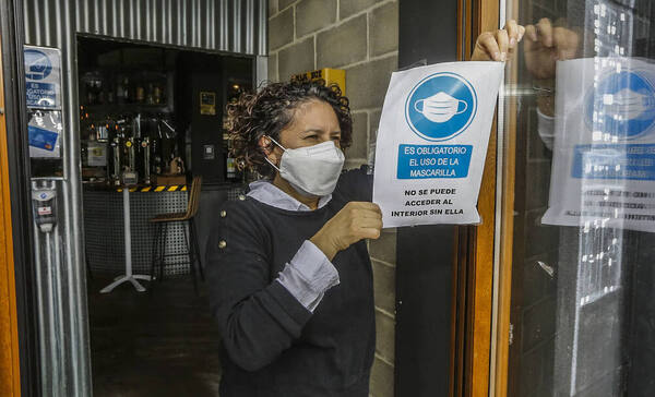 Una mujer retira el cartel del uso obligatorio de la mascarilla en el bar Prebistro, en Suances. Foto: Luis Palomeque.